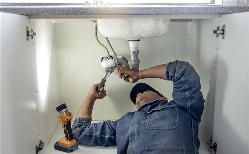 Plumber repairing pipes beneath a bathroom sink in Fremont